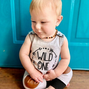 Baby in Wild One romper sitting in front of blue door