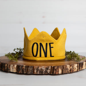 Gold knitted crown with ONE in black script lettering and gold accents